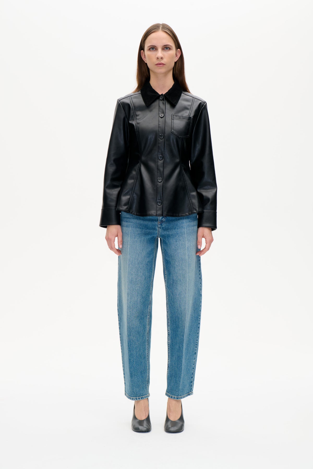 Framifrån: modell i svart jacka med knäppning fram, krage i kontrastfärg och bröstficka, blå jeans och svarta skor.