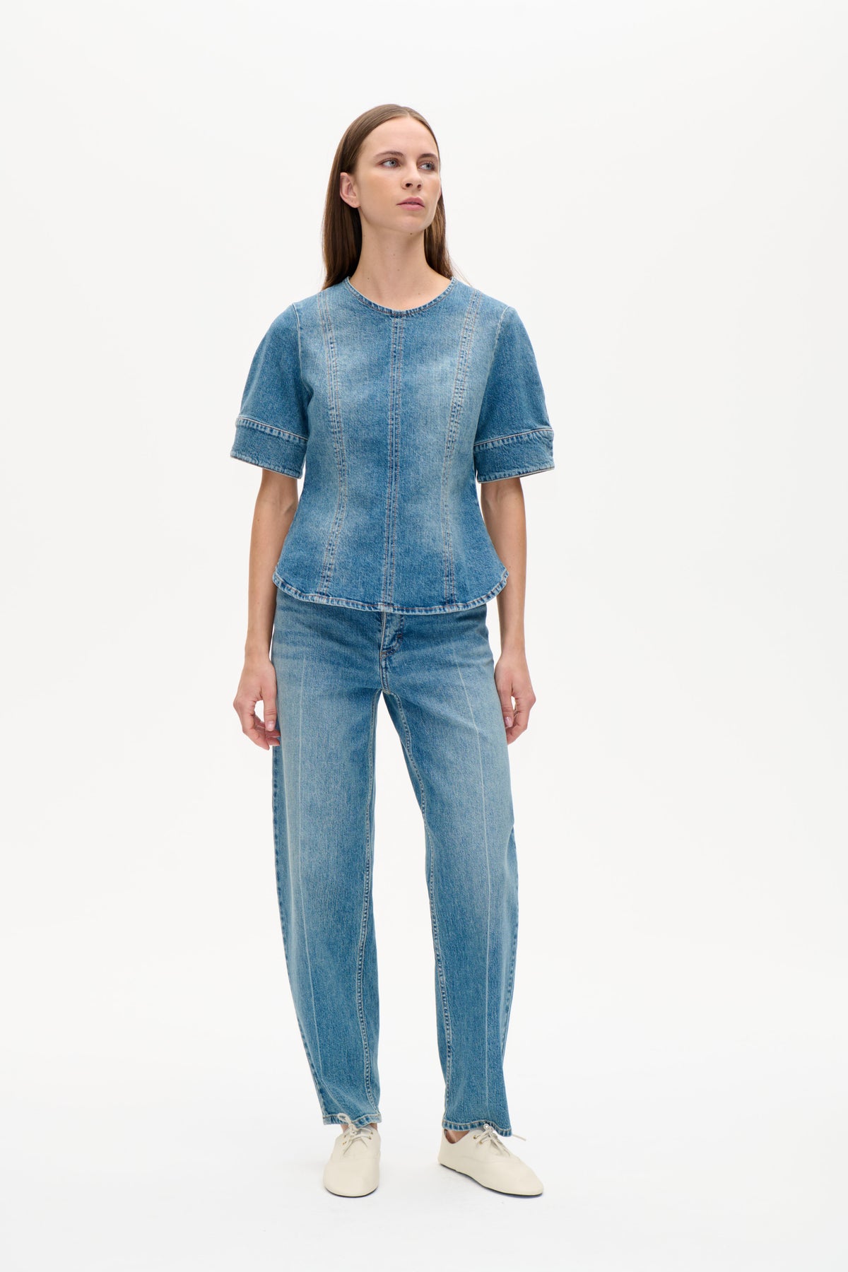 Framifrån: modell i blå denimtopp, kortärmad med rund halsringning och tydliga vertikala panelsömmar, matchad med jeans.