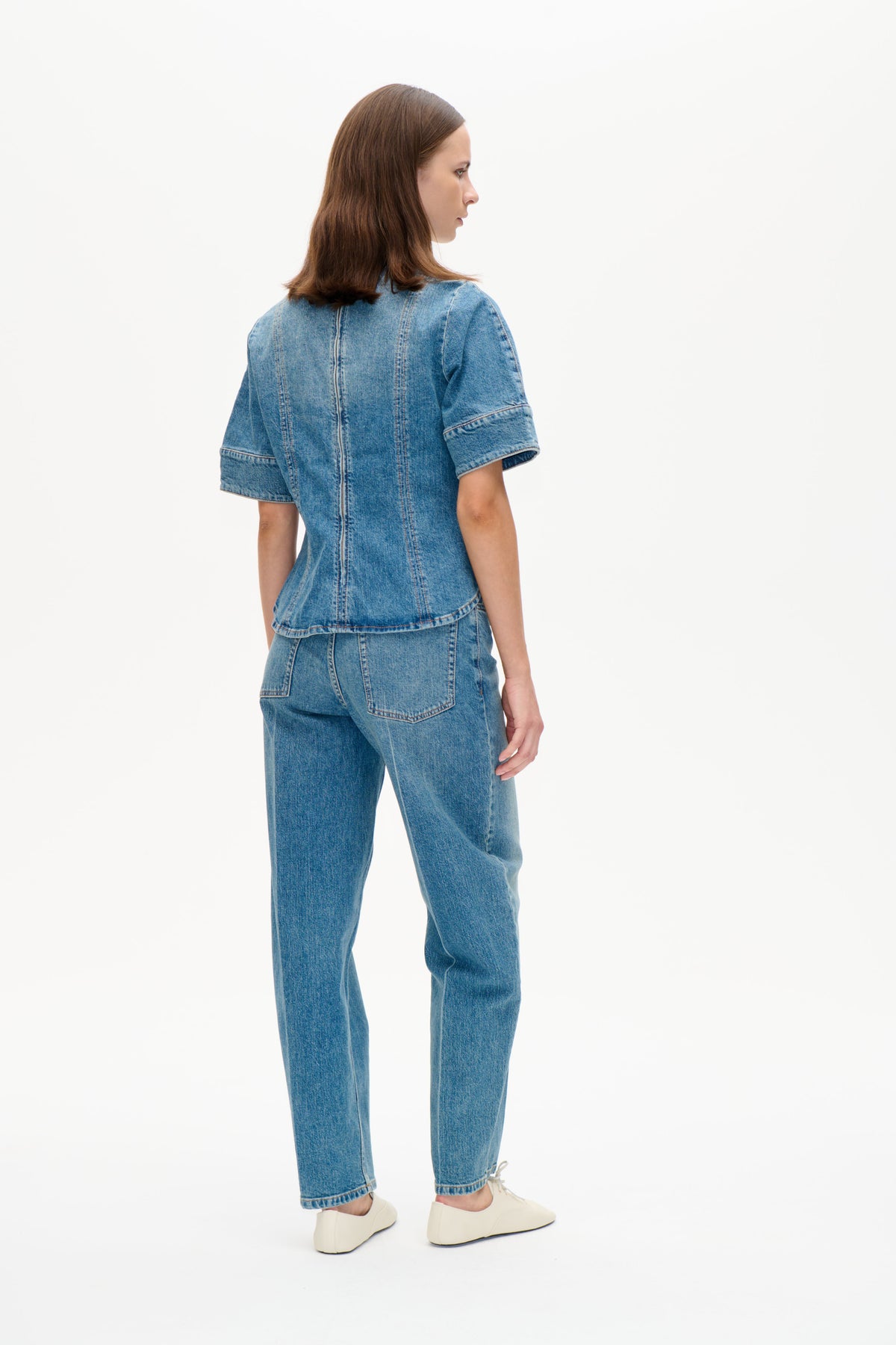 Modell i blå, kortärmad denimtopp och matchande jeans, visad bakifrån och i profil mot vit bakgrund.
