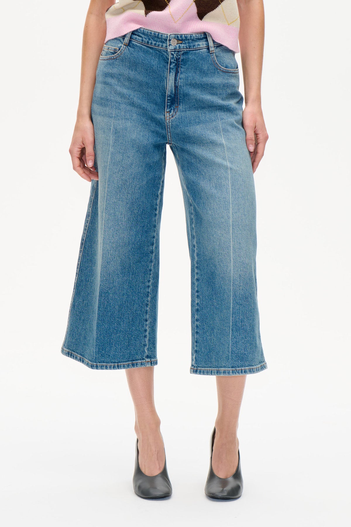 Framifrån: vida, croppade blå jeans med blekt tvätt, kombinerade med en rosa- och krämfärgad mönstrad stickad topp.