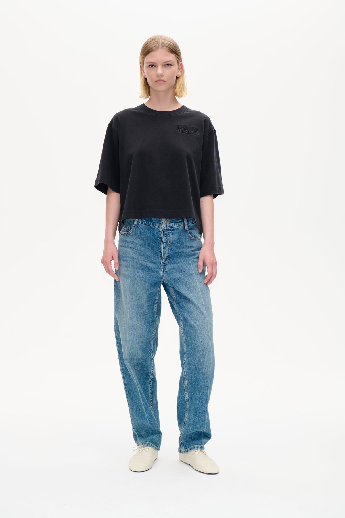 Framifrån: modell i en oversized kolgrå t-shirt med ton-i-ton Baum und Pferdgarten-text på bröstet och blå jeans.