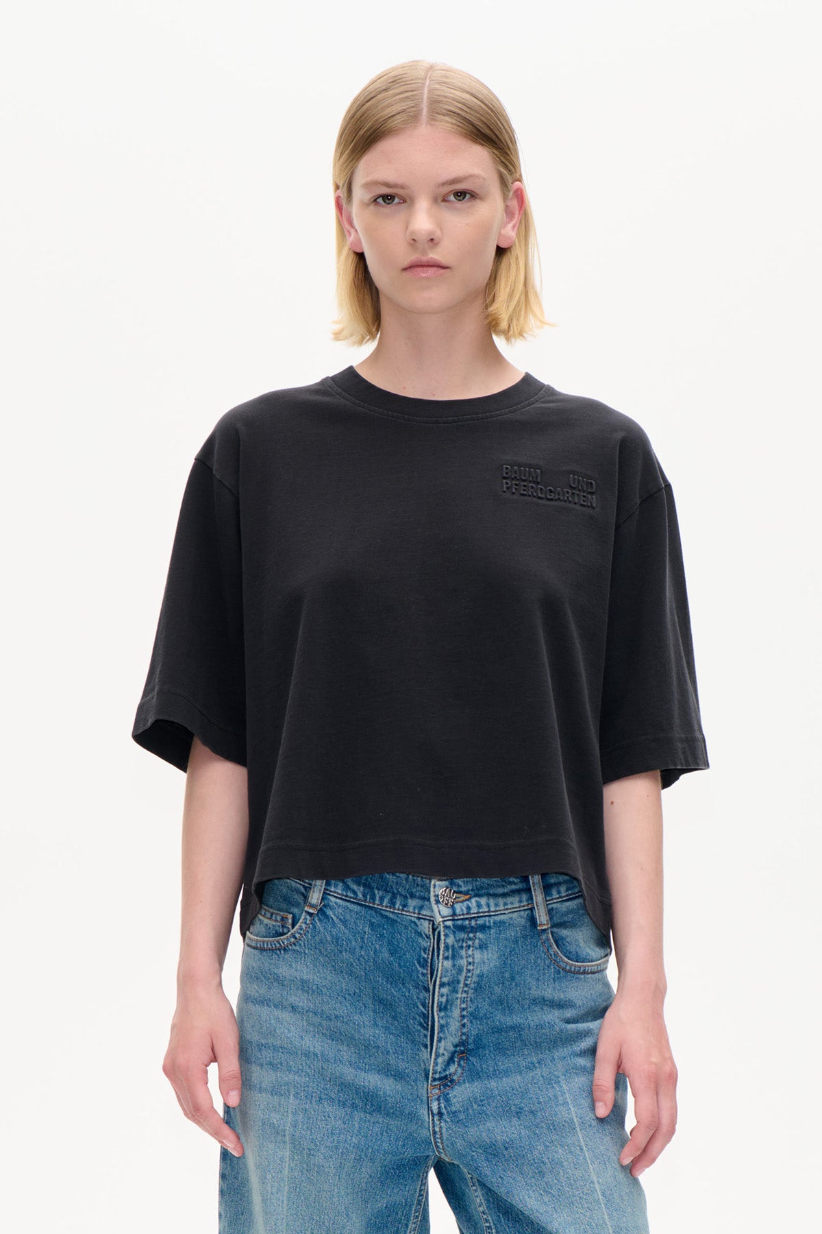 Framifrån: svart croppad oversized kortärmad t-shirt med diskret upphöjd text över bröstet, kombinerad med blå jeans.