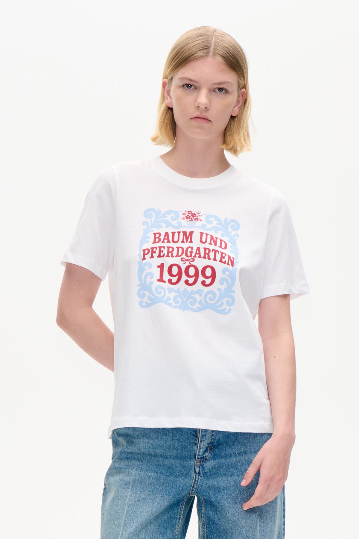 Vit kortärmad t-shirt med blå ornamentram och röd Baum und Pferdgarten 1999-print, visad framifrån.