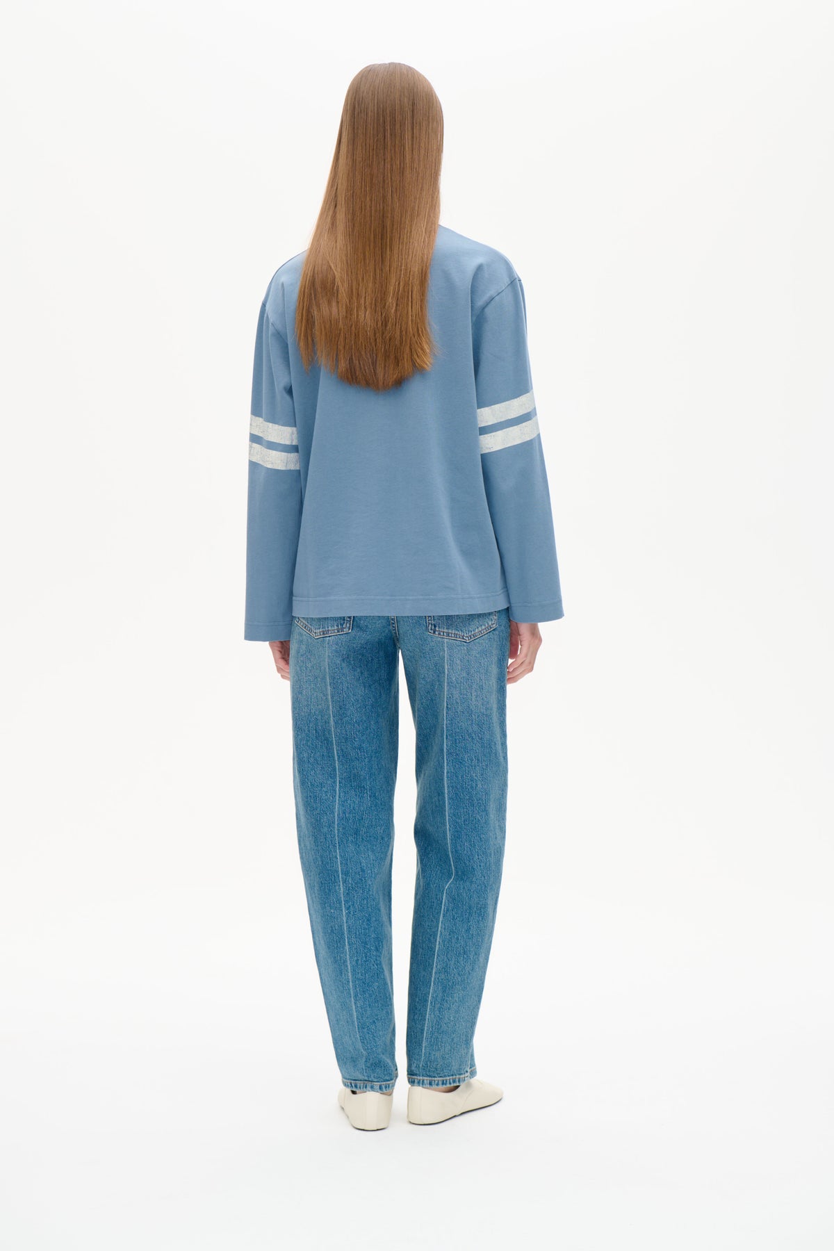 Bakifrån: modell i ljusblå långärmad sweatshirt med vita ränder på ärmarna och blå jeans.