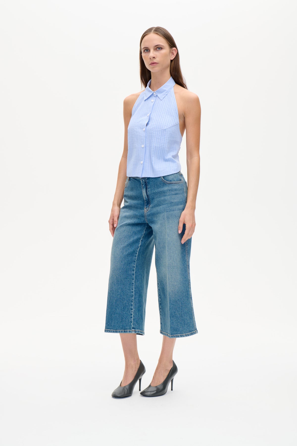 Modell bär ljusblå smalrandig ärmlös topp med knäppning fram, spetsig krage och vida blå jeans.