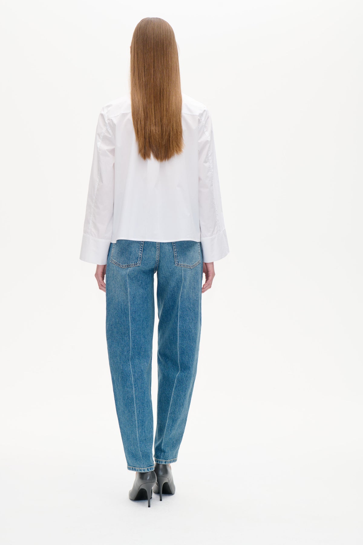Bakifrån: en modell som bär en vit långärmad blus med vida manschetter och blå jeans med påsydda bakfickor.