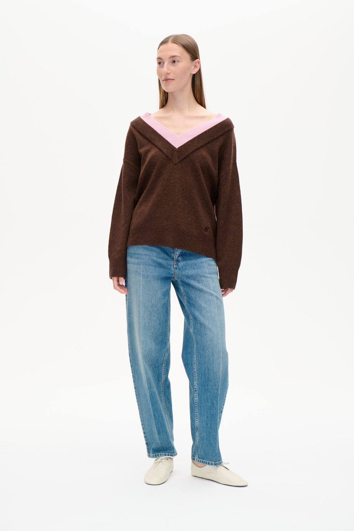 Framsida på en brun stickad tröja med bred rosa V-ringning, kombinerad med ljusblå jeans.