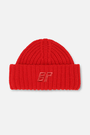 Närbild av en röd tjockstickad mössa med uppvikt mudd och ton-i-ton broderat BP-monogram.