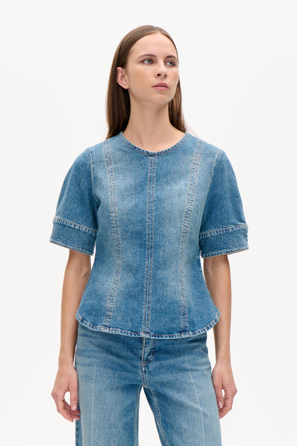 Framifrån: en blå denimtopp med rund halsringning, korta vida ärmar och vertikala panelsömmar, stylad med jeans.