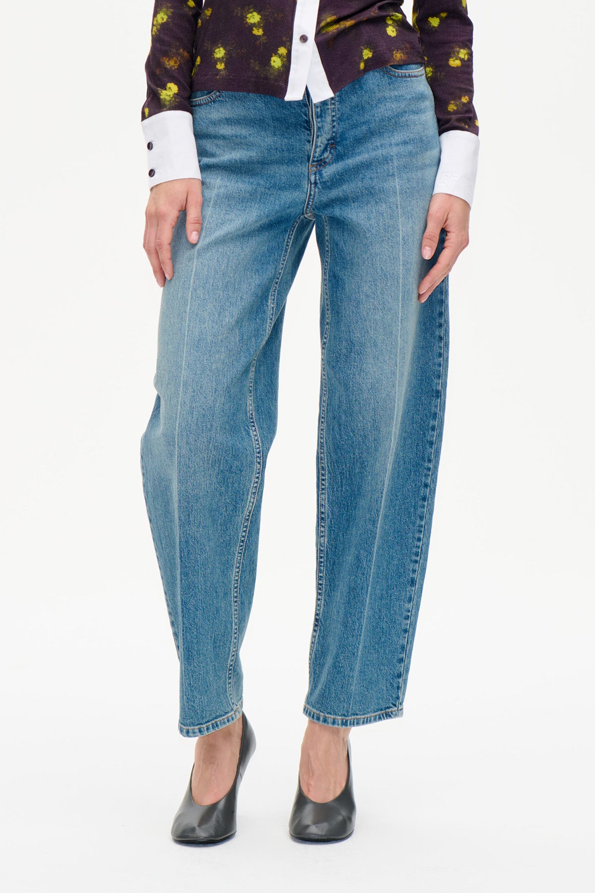 Detaljbild framifrån av blå jeans med raka ben och avblekt tvätt, stylade med en mörk blommig topp och svarta klackar.