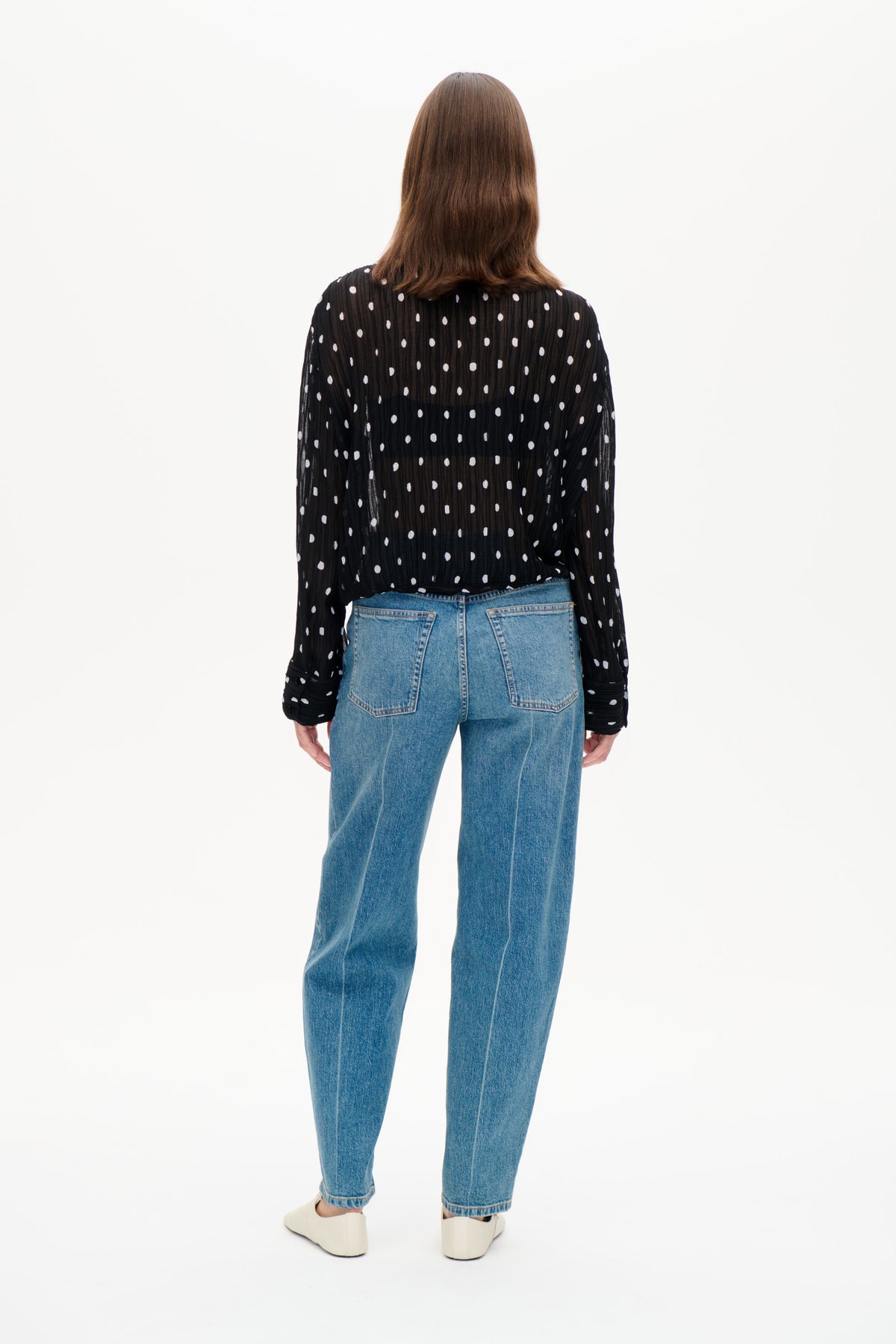 Ryggvy av en svart transparent långärmad blus med vita prickar, kombinerad med blå jeans.