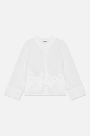 Framifrån en vit långärmad blus med rund hals, blanka knappar, vida manschetter och oversized rosettdetaljer i midjan.