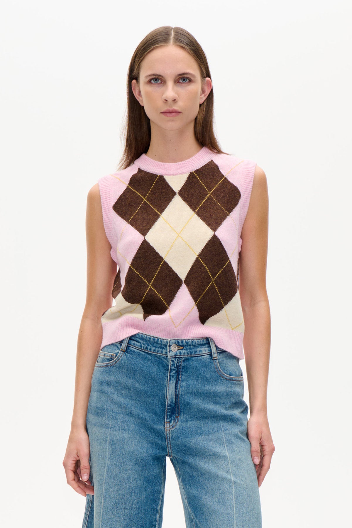 Framifrån en rosa ärmlös stickad väst med creme- och mörkbruna argyle-romber, matchad med blå jeans.