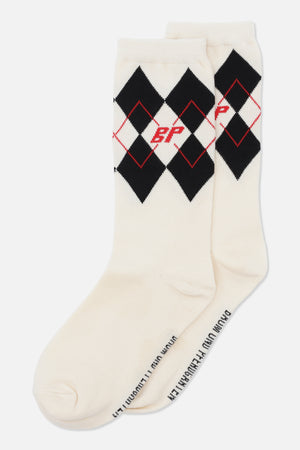 Par krämfärgade crewstrumpor med svarta argyle-romber, tunna röda rombkonturer och ett rött monogram vid muddarna.