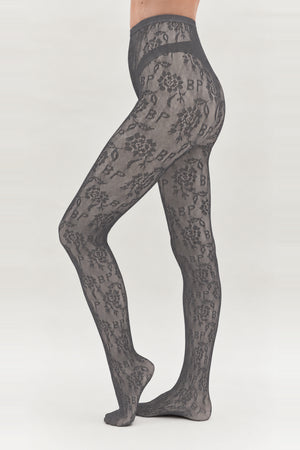 Sheer charcoal-grey tights with an all-over floral and BP monogram pattern, shown on a model from waist to feet.